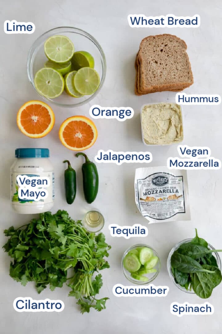 vegan green goddess sandwich ingredients: limes, oranges, vegan mayo, jalapeno, tequila, cilantro, bread, hummus, vegan mozzarella, cucumbers and spinach.