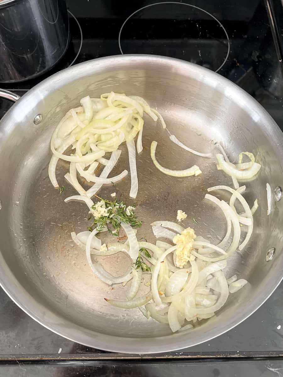 translucent onion slices with fresh garlic and thyme added to pan