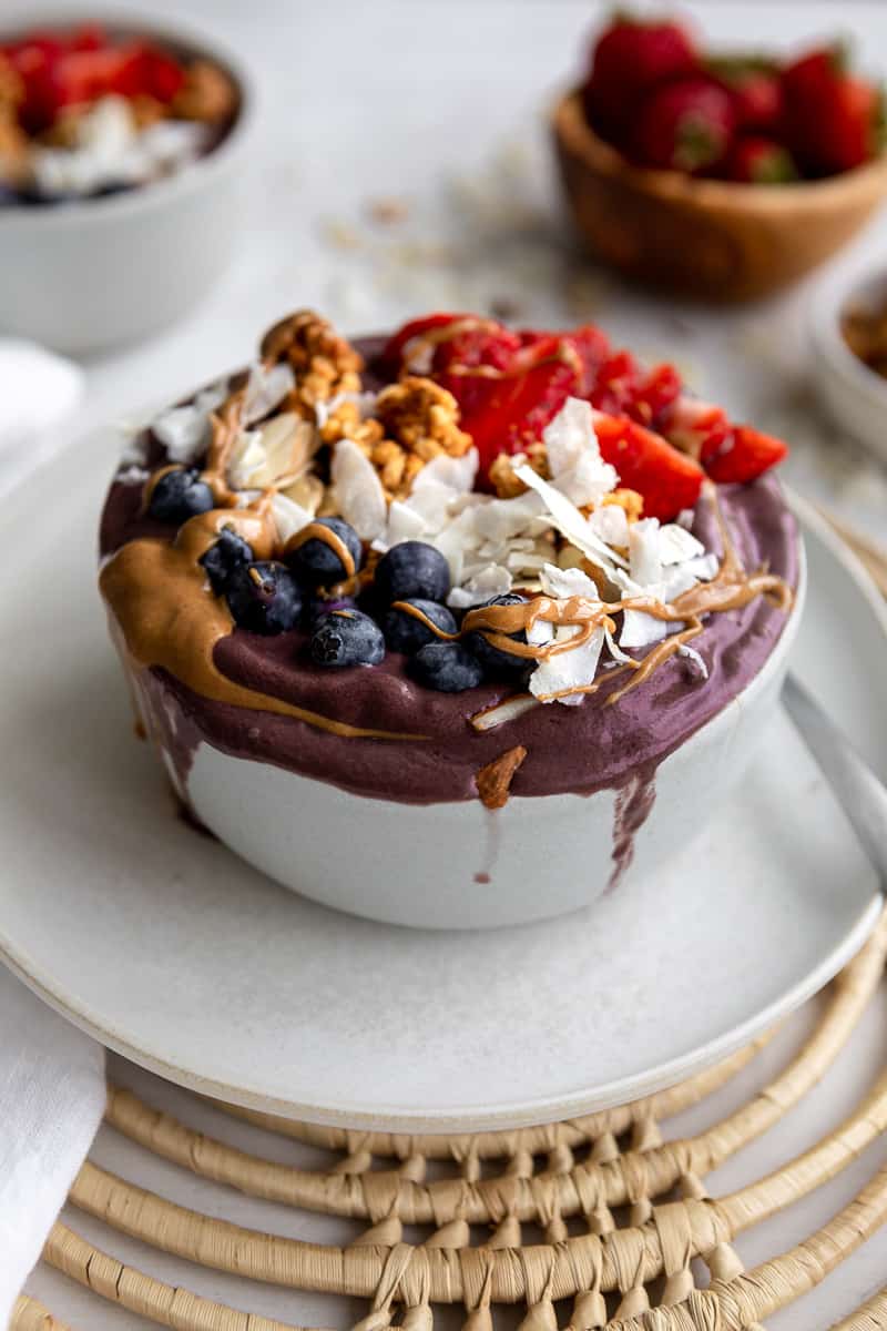 Thick purple acai topped with peanut butter drizzles, blueberries, coconut flakes, granola and strawberries
