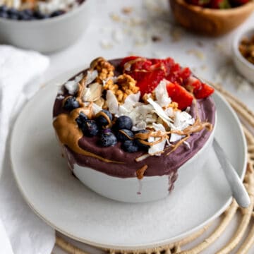 purple acai smoothie bowl with blueberries, coconut flakes, strawberries and peanut butter drizzle.