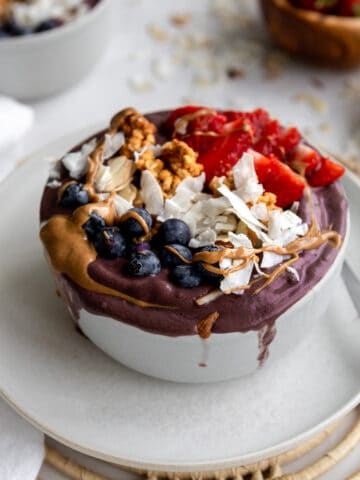 purple acai smoothie bowl with blueberries, coconut flakes, strawberries and peanut butter drizzle