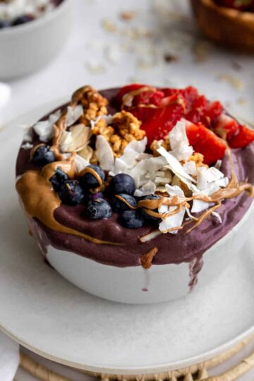 purple acai smoothie bowl with blueberries, coconut flakes, strawberries and peanut butter drizzle.