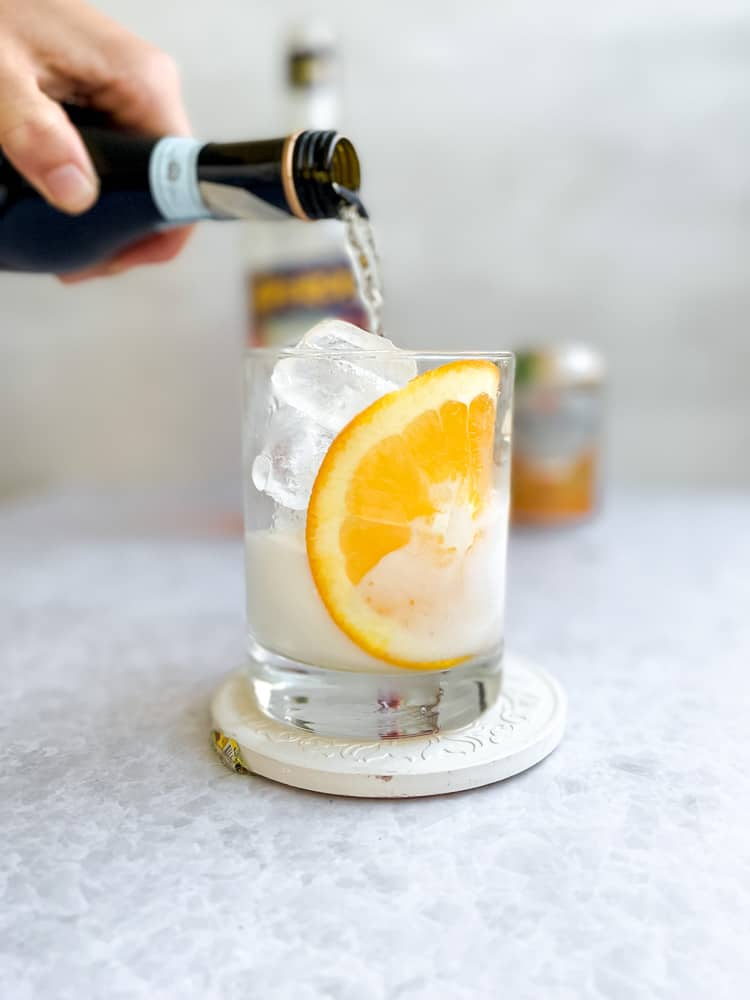 Pouring prosecco into a glass with ice and an orange slice