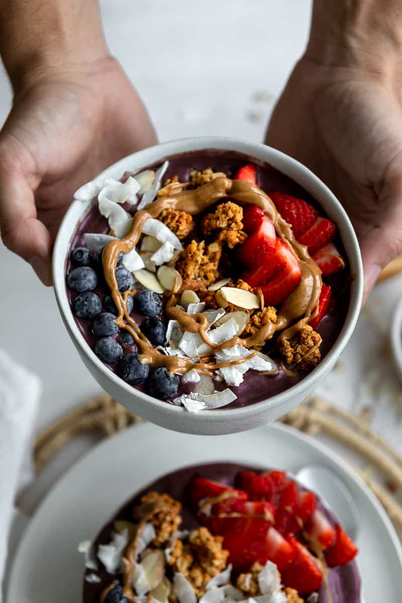 Hands holding an acai bowl with peanut butter drizzle and fresh berries