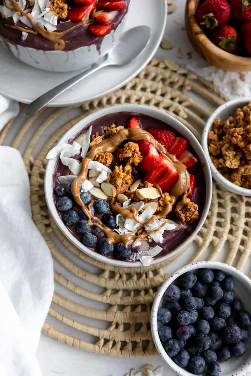 Smoothie bowl decorating with fresh berries, nuts, granola and peanut butter drizzle