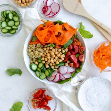 salad with rainbow colors - carrots, quinoa, chickpeas, cucumbers, greens, radishes, and tomatoes