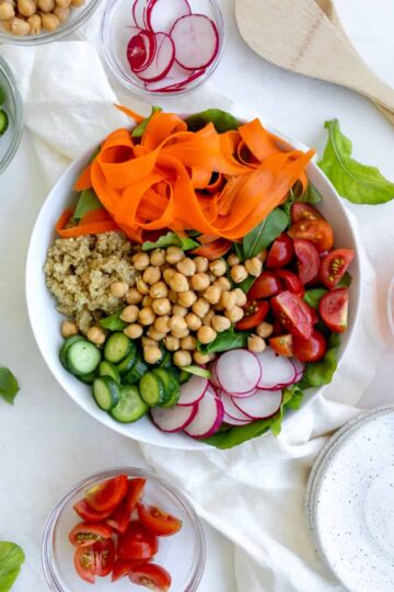 salad with rainbow colors - carrots, quinoa, chickpeas, cucumbers, greens, radishes, and tomatoes.