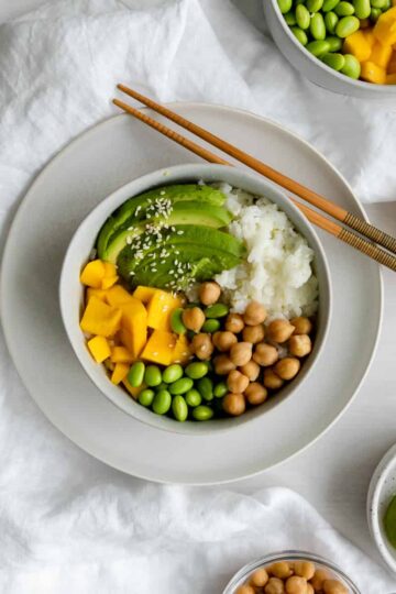 chickpea buddha bowl with mango, avocado, rice, edamame and chopsticks.