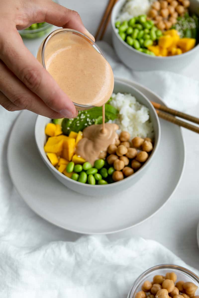 smooth peanut sauce pouring onto a rice bowl with veggies