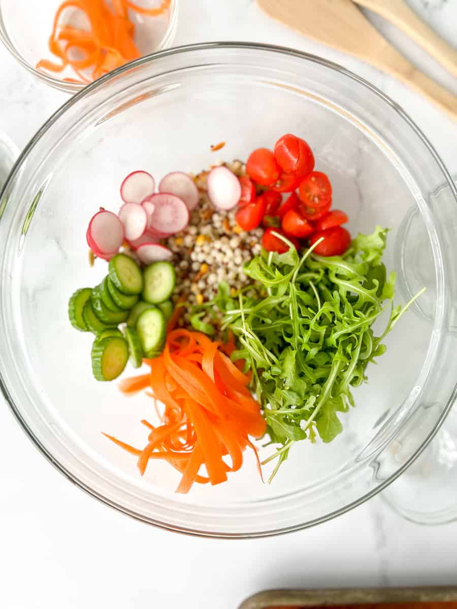 Rainbow salad ingredients: grain (like couscous of quinoa), tomatoes, arugula, carrots, cucumber and radishes