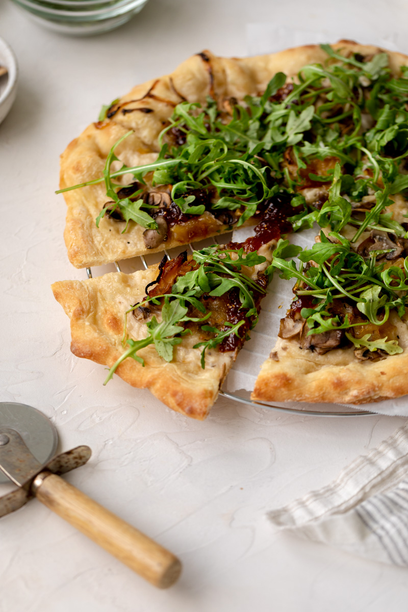 slice of vegan pizza with white sauce, mushrooms, caramelized onions, fig jam and arugula