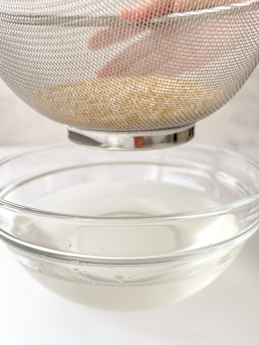 Rice in a mesh sieve over a bowl of water
