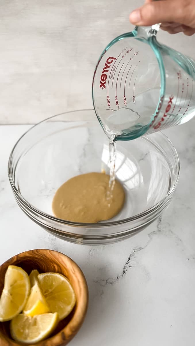 Water pouring into a bowl with tahini