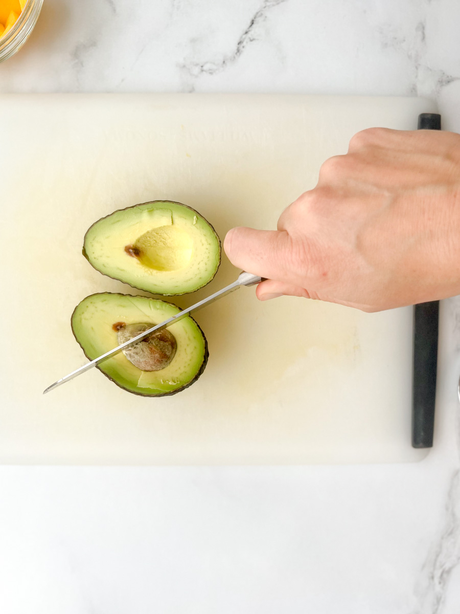avocado sliced in half, with a chef's knife cutting into the pit of the avocado