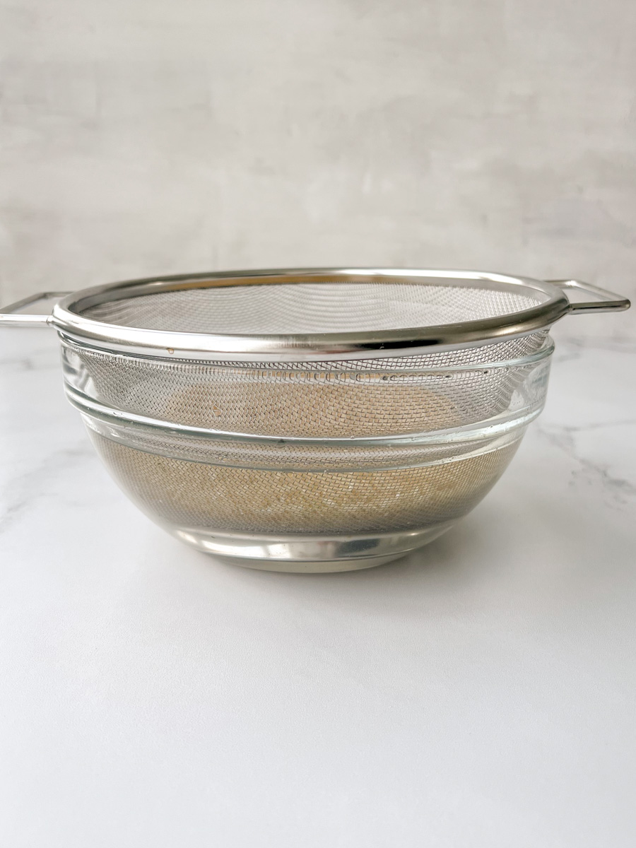 Mesh sieve with rice in a clear bowl of water. 