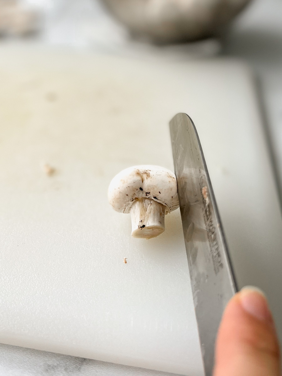 slicing a mushroom on its side, knife parallel to the stem. 