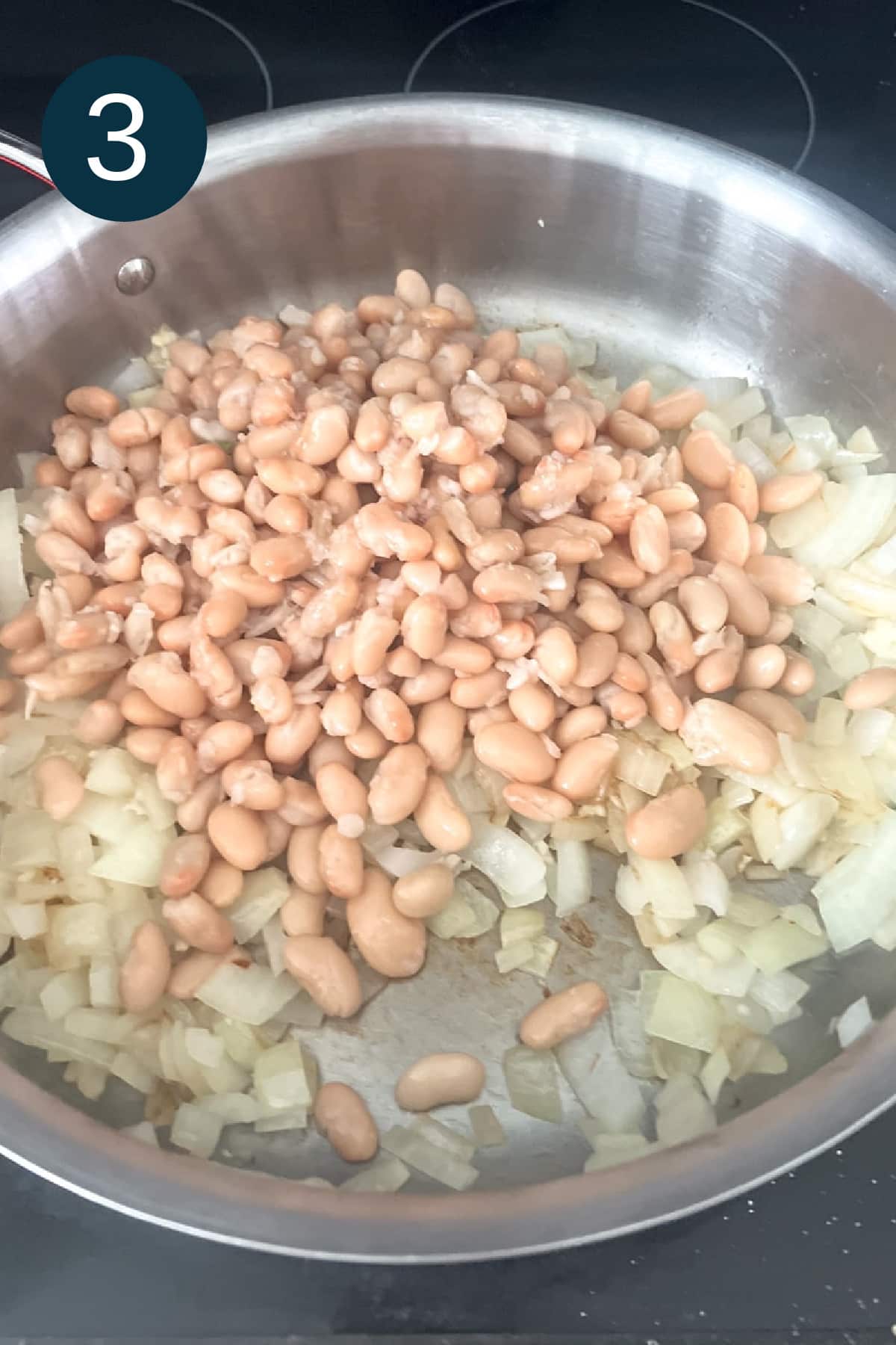 white beans and onions in pot on a stove.