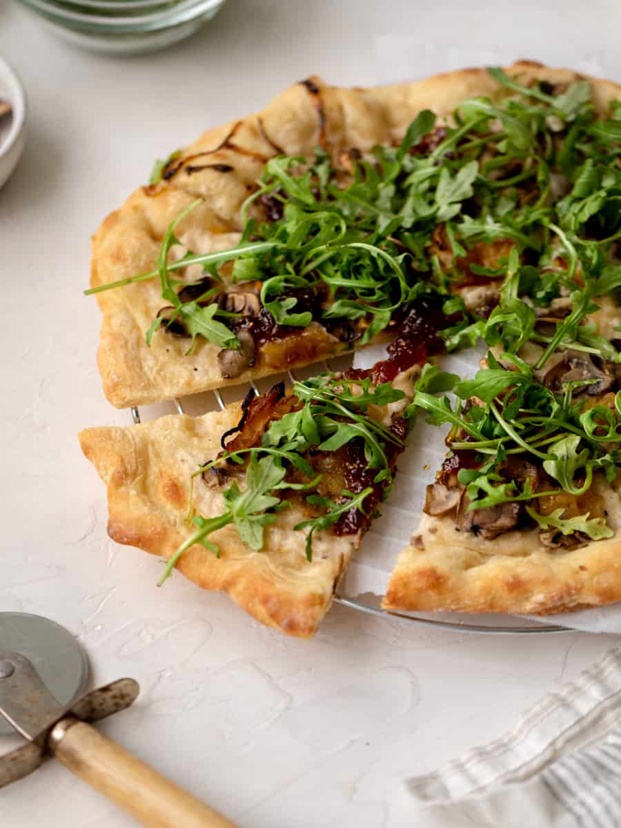 vegan arugula pizza with a pizza cutter next to it.