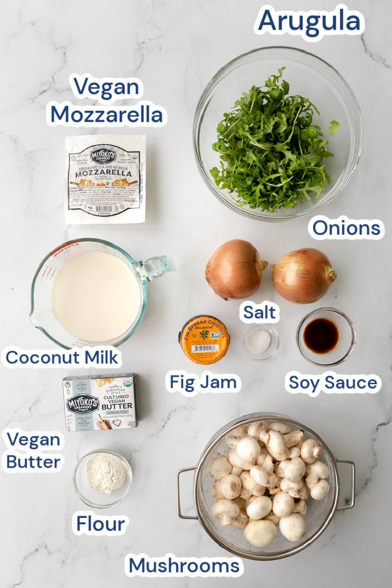 ingredients for vegan mushroom pizza: Aaugula, vegan mozzarella, onions, soy sauce, coconut milk, fig jam, vegan butter, flour, mushrooms, salt.