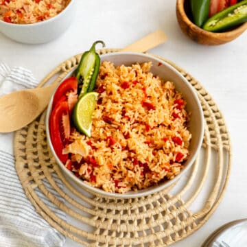 mexican rice in a bowl sprinkled with tomatoes and garnished with jalapeno and lime.