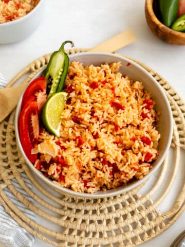 mexican rice in a bowl sprinkled with tomatoes and garnished with jalapeno and lime