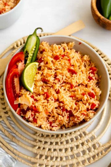 mexican rice in a bowl sprinkled with tomatoes and garnished with jalapeno and lime.