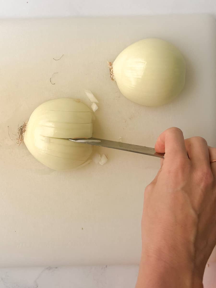 half an onion on a cutting board, knife pointing toward root, slicing toward cutting board