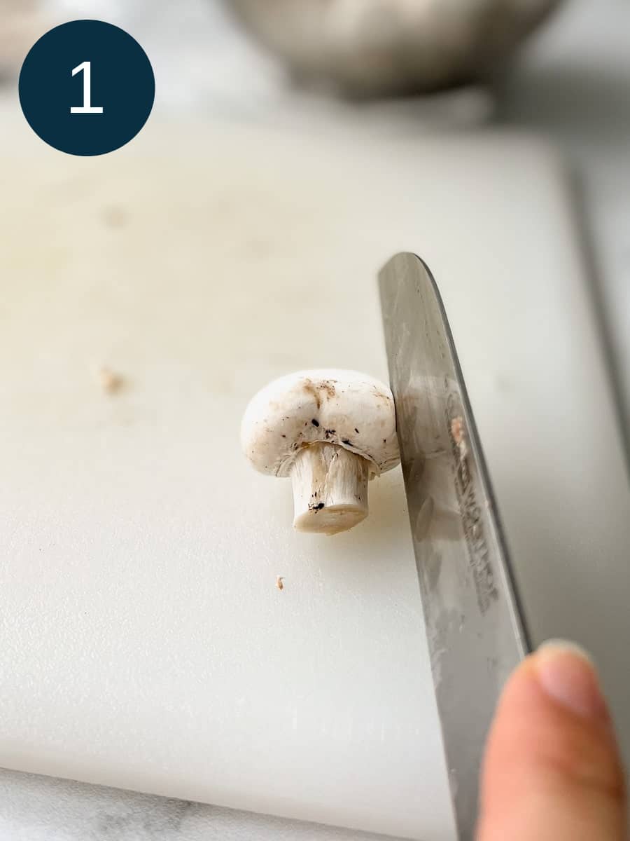 slicing a mushroom on a white chopping board.