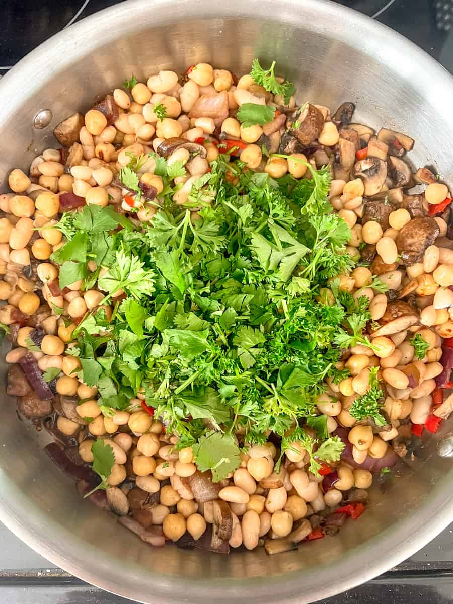 large pan with sauteed onions and mushrooms, chickpeas, parsley and cilantro
