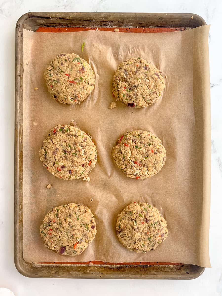 6 unbaked chickpea falafel burger patties on a lined baking sheet