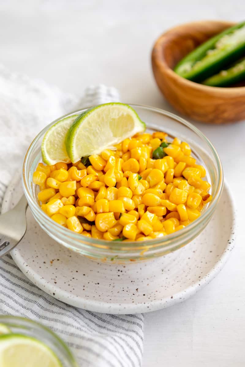 mexican street corn in a bowl with jalapenos, garnished with lime