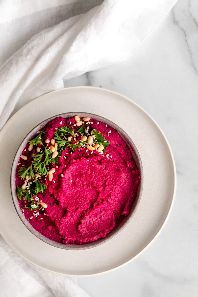 overhead view of hot pink hummus in a bowl garnished with parsley and pine nuts