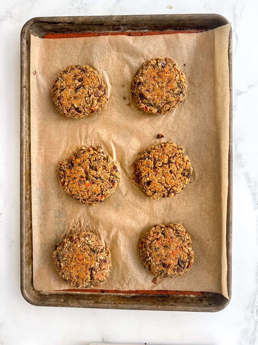 6 baked chickpea falafel burgers on a lined baking sheet with slightly crispy tops 