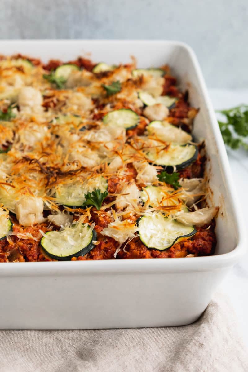 lasagna in a casserole dish topped with zucchini and lightly browned vegan parmesean