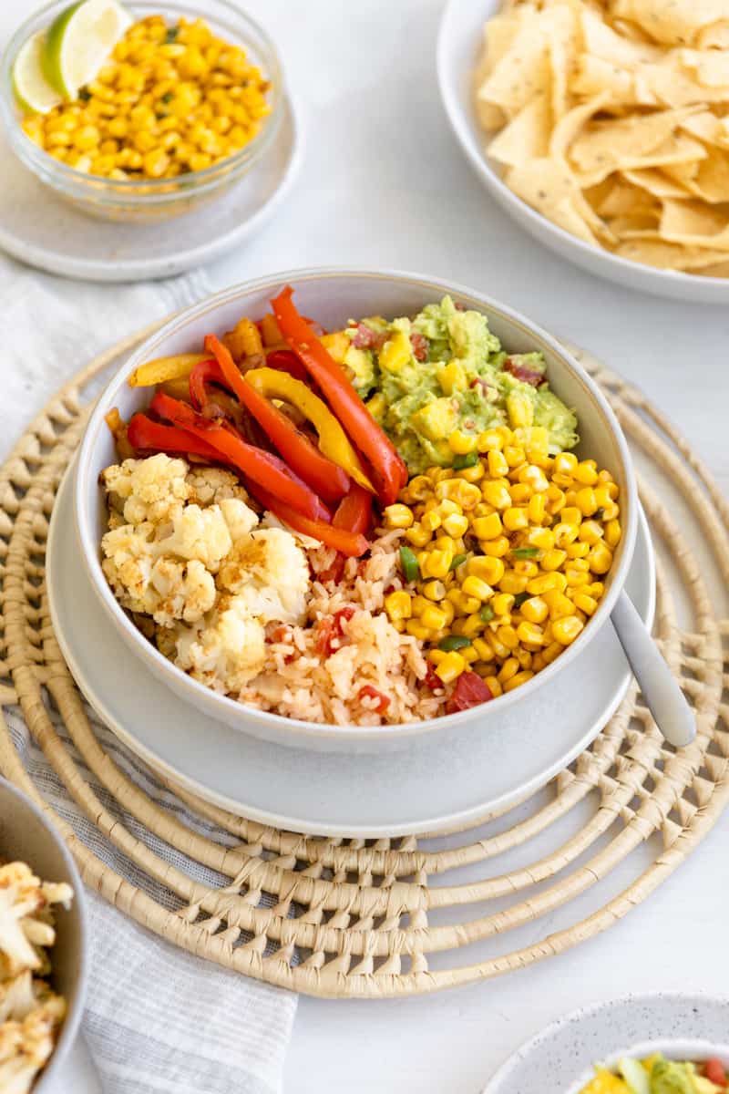 bowl with red mexican rice, roasted cauliflower, bell peppers, guacamole, and street corn kernels