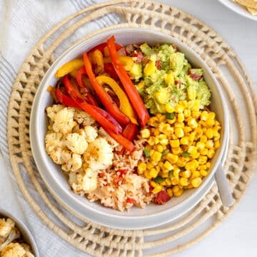 bowl with roasted cauliflower, sauteed red and yellow peppers, guacamole, corn and red mexican rice