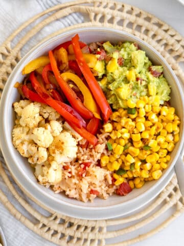 bowl with roasted cauliflower, sauteed red and yellow peppers, guacamole, corn and red mexican rice