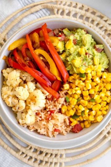 bowl with roasted cauliflower, sauteed red and yellow peppers, guacamole, corn and red mexican rice.