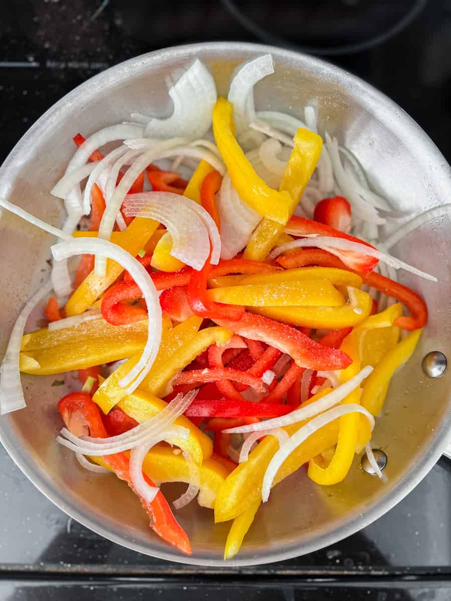 red and yellow bell peppers and white onion slices in a frying pan with salt
