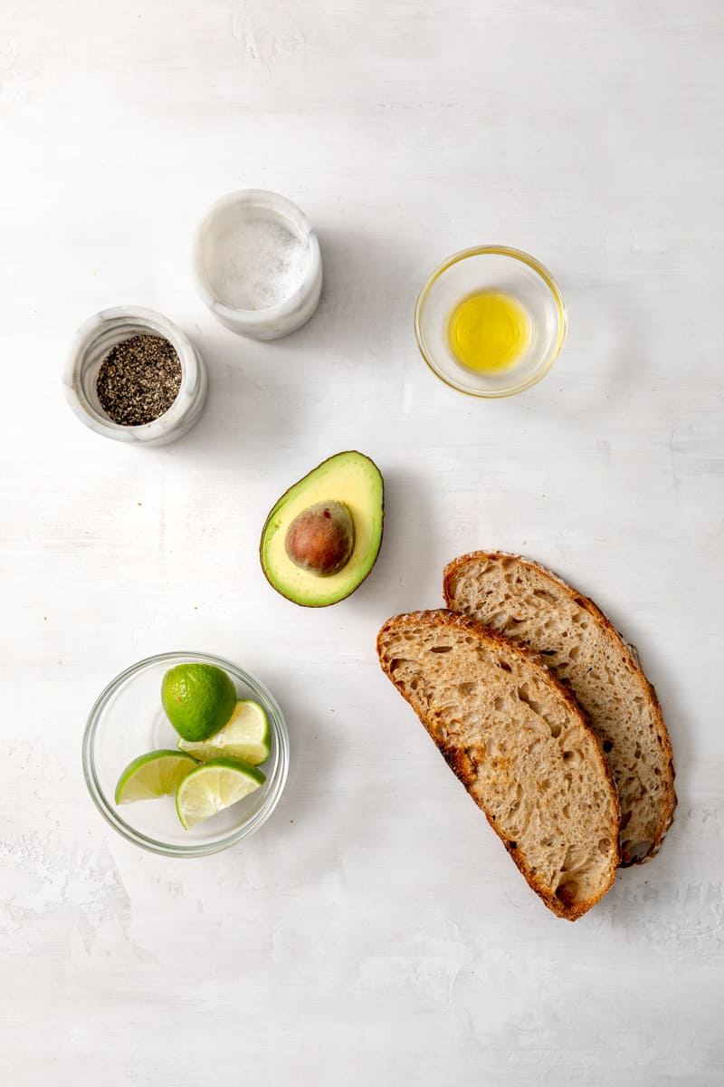overhead view of avo toast ingredients - salt, pepper, olive oil, avocado, limes, and bread slices