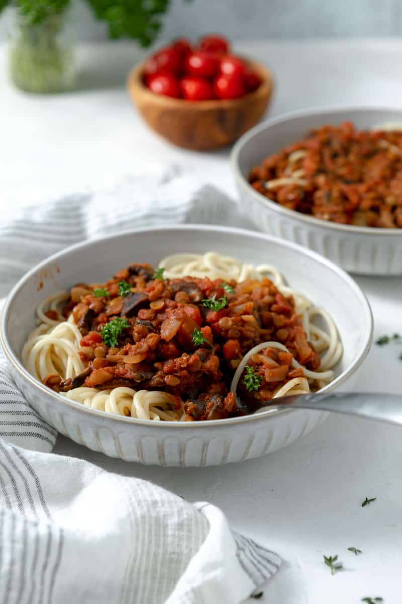 close up of a bowl of spaghetti with lentil bolognese sauce and a fork