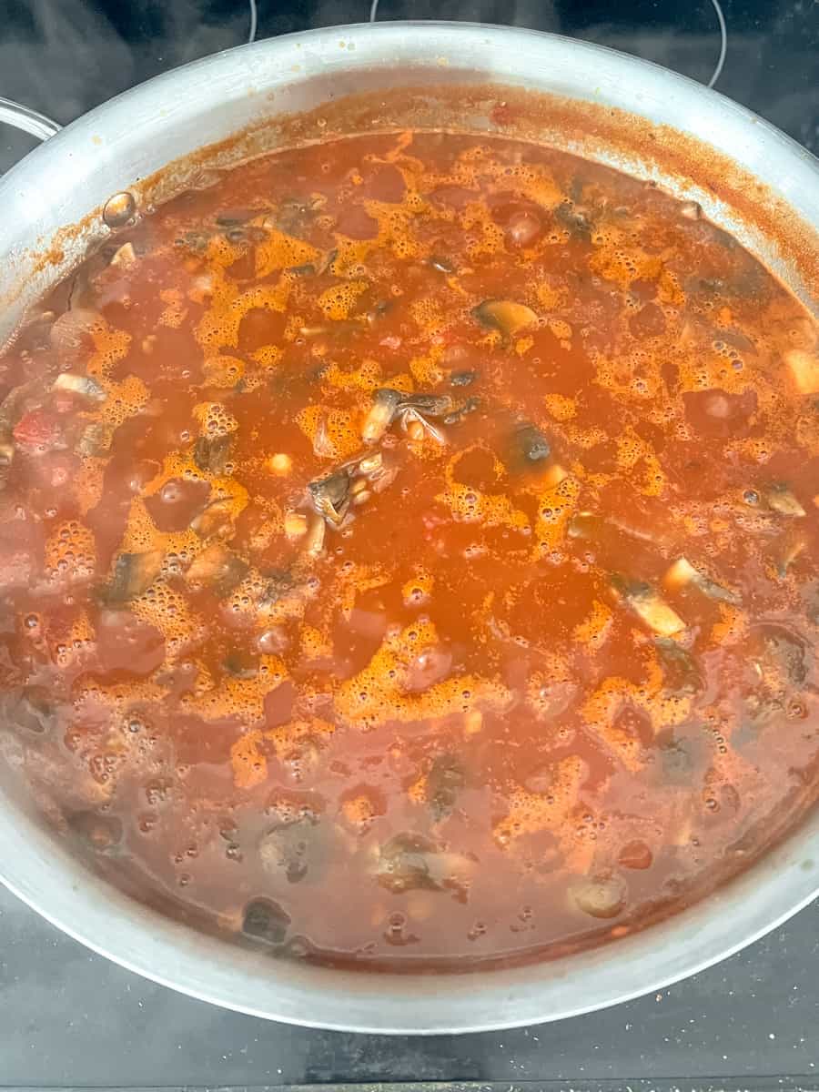 simmered vegan bolognese sauce - some bubbles and liquid on top of the pan, with thick vegetables and lentils underneath. 