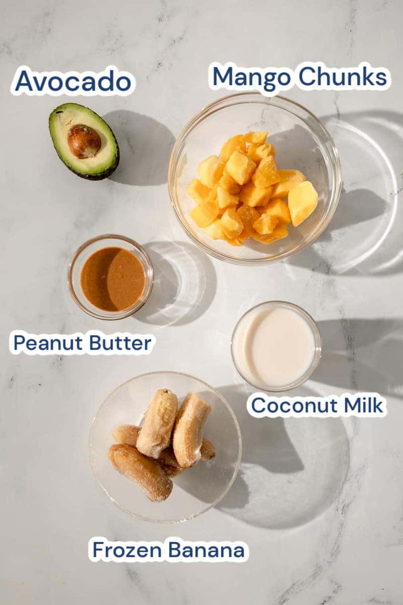 Ingredients for a mango avocado smoothie, peanut butter, mango chunks, coconut milk, frozen banana and avocado.