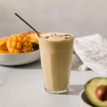 mango avocado smoothie in a glass with a metal straw.