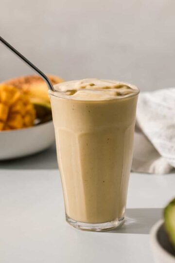 mango avocado smoothie in a glass with a metal straw.