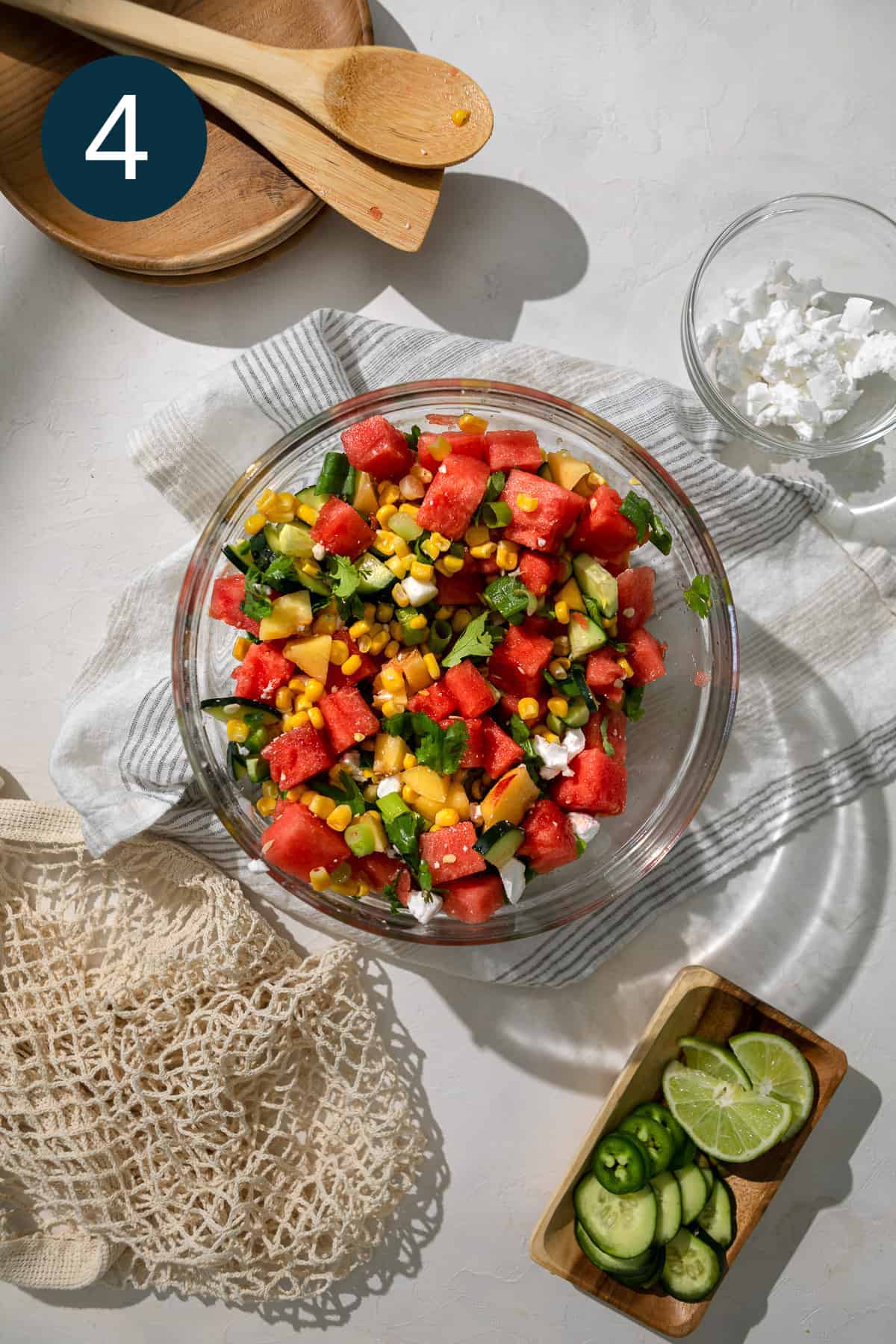 water melon vegan feta and peaches in a bowl surrounded by wooden utensils and lime wedges.