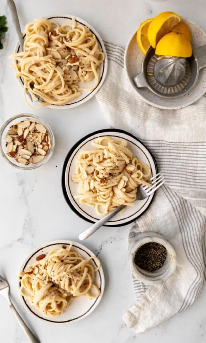 vegan bean pasta sauce twirled on a fork over plates with lemons on the side.